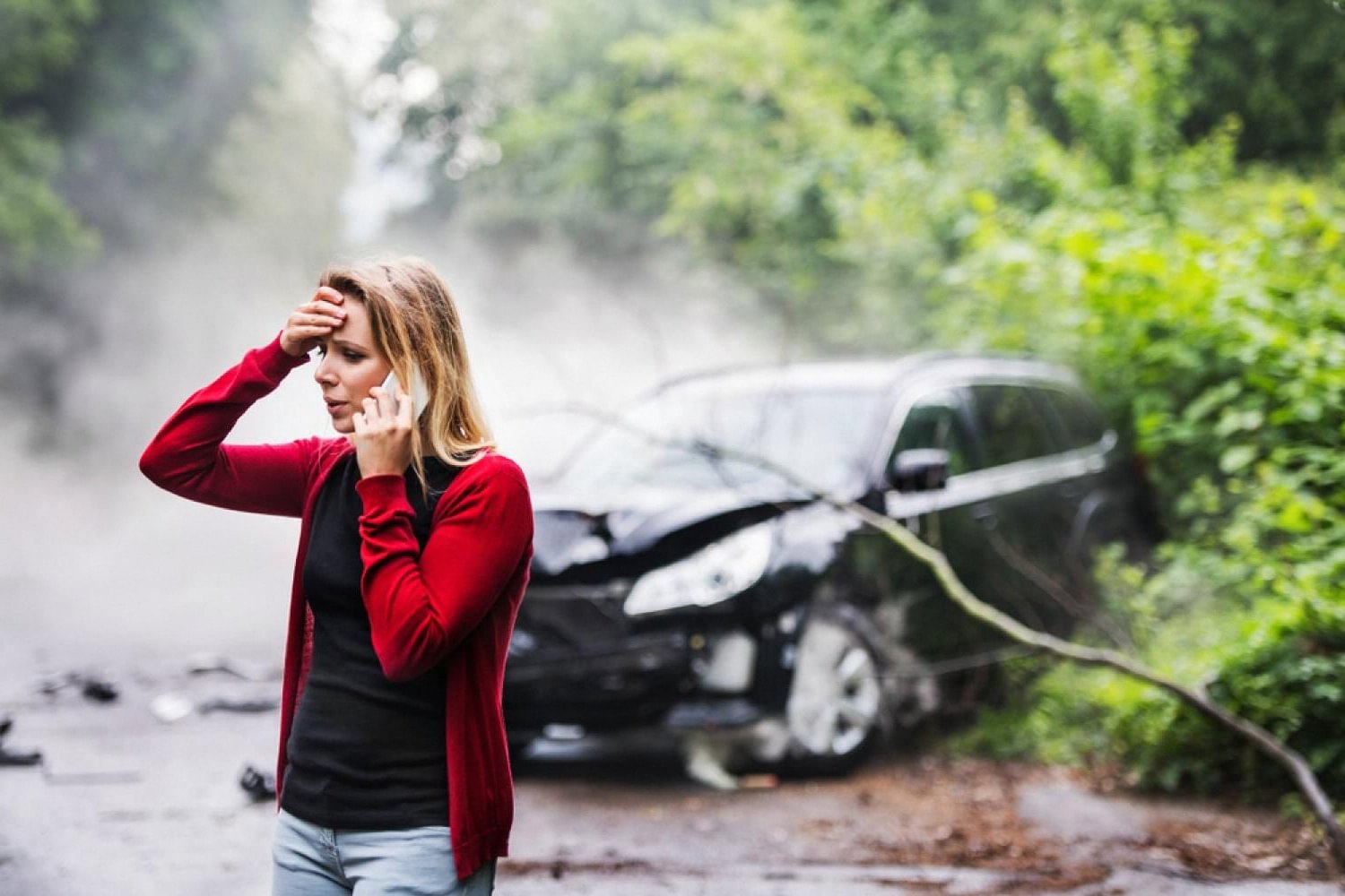 Woman on the phone next to a damaged car after an accident, illustrating a car insurance claim in Dubai