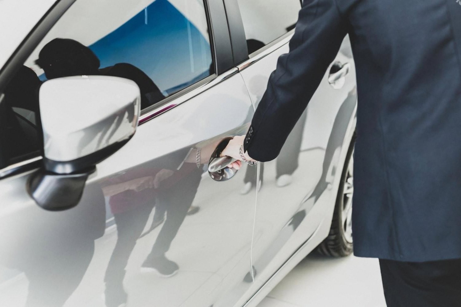 Chauffeur in a dark suit opening the passenger door of a white luxury sedan
